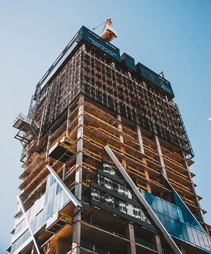 high-rise-construction-site Low-angle view of a multi-story building under construction with exposed concrete, safety scaffolding, and a tower crane at the top.
